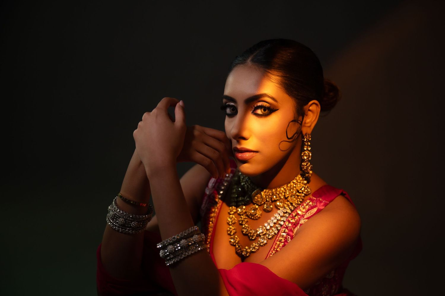 South Asian bride in pink lehenga with gold jewelry poses in warm dramatic studio lighting.