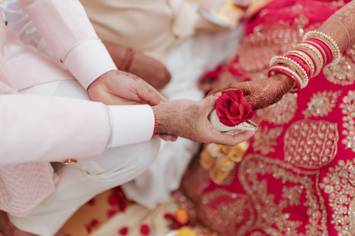 Close-up of hands during traditional Indian wedding ritual with red rose petals.