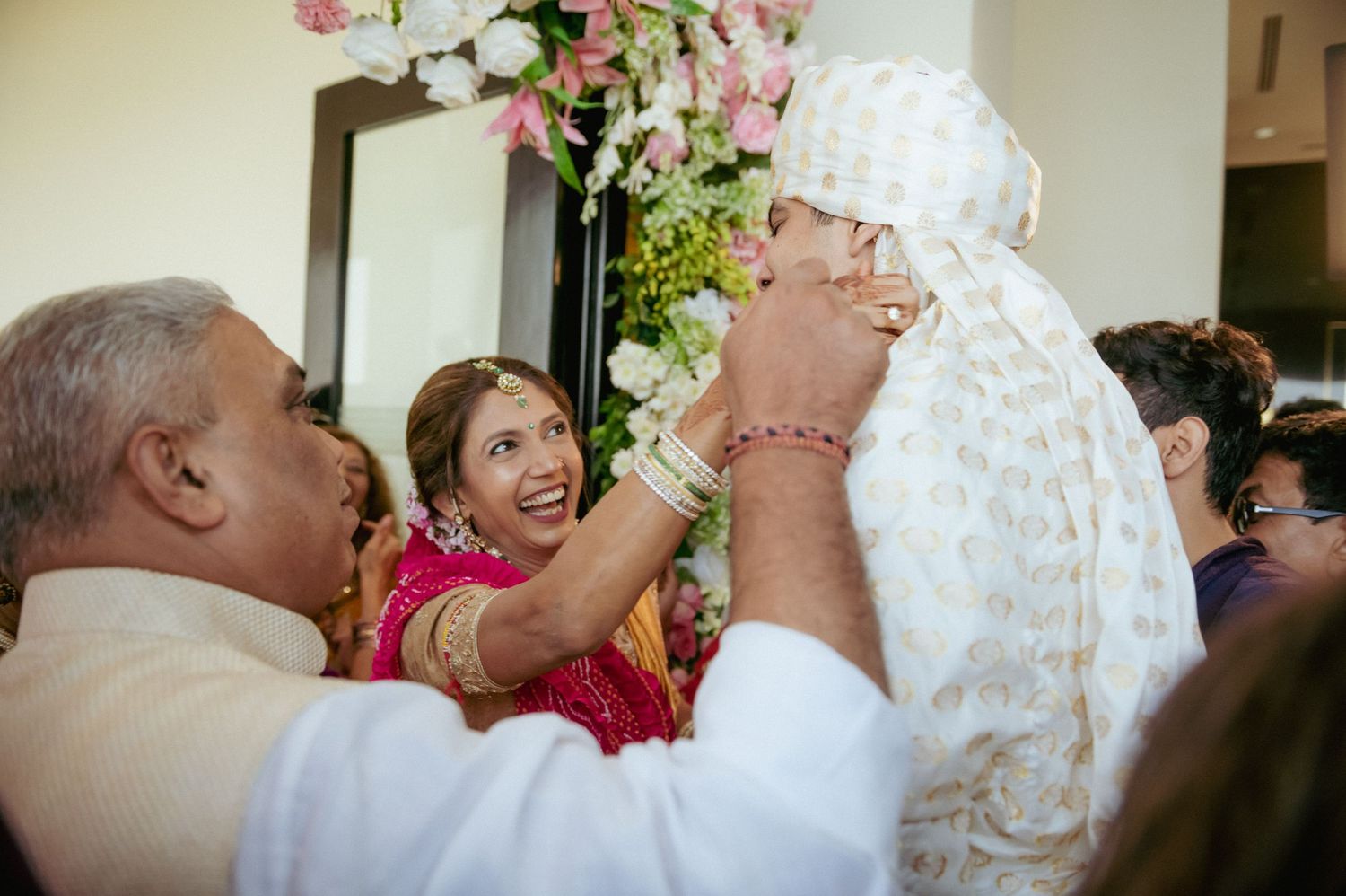 Elderly man blesses Indian groom in white sherwani during traditional wedding ceremony.