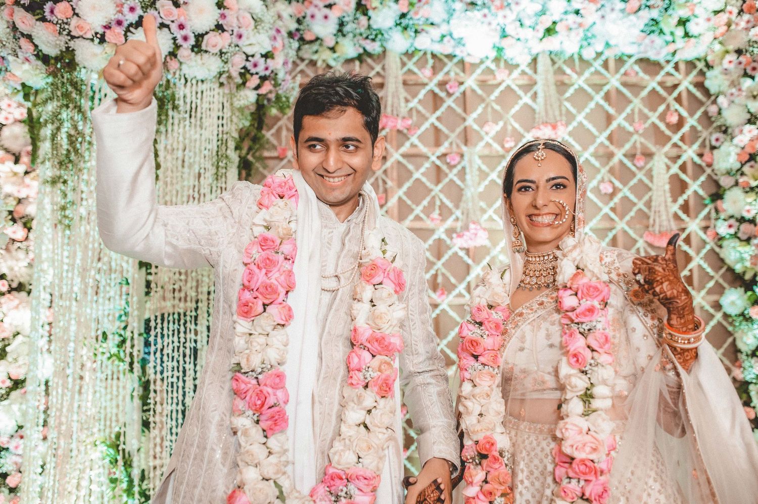 Happy Indian bride and groom celebrating after wedding ceremony with pink floral garlands and decorations.
