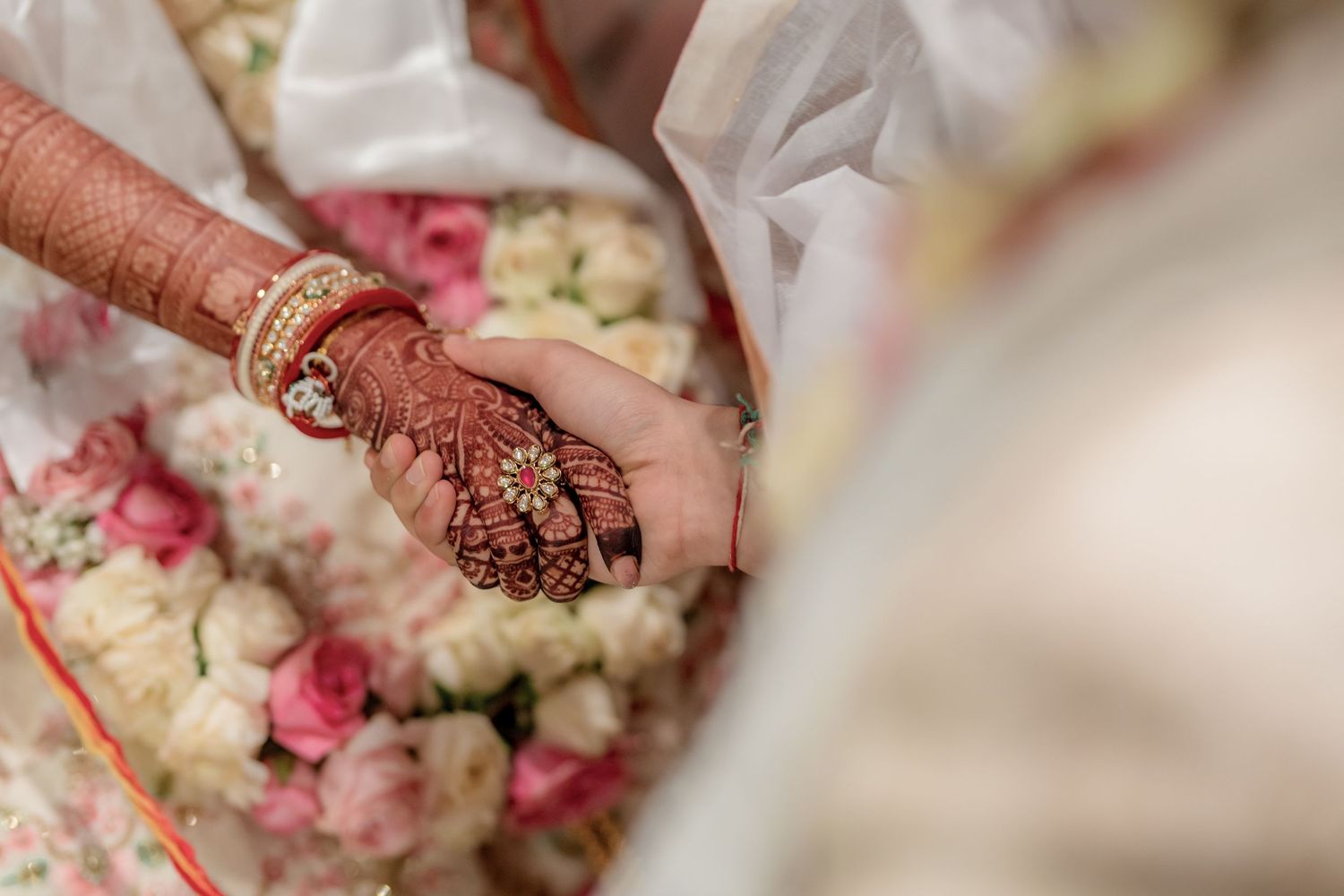 Close-up of bride's henna-adorned hands holding flowers at Indian wedding ceremony.