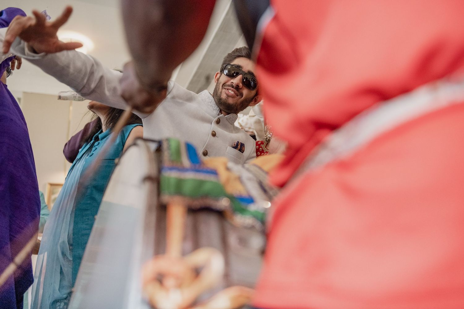 Man in sunglasses smiling surrounded by colorful fabric at Indian wedding celebration.