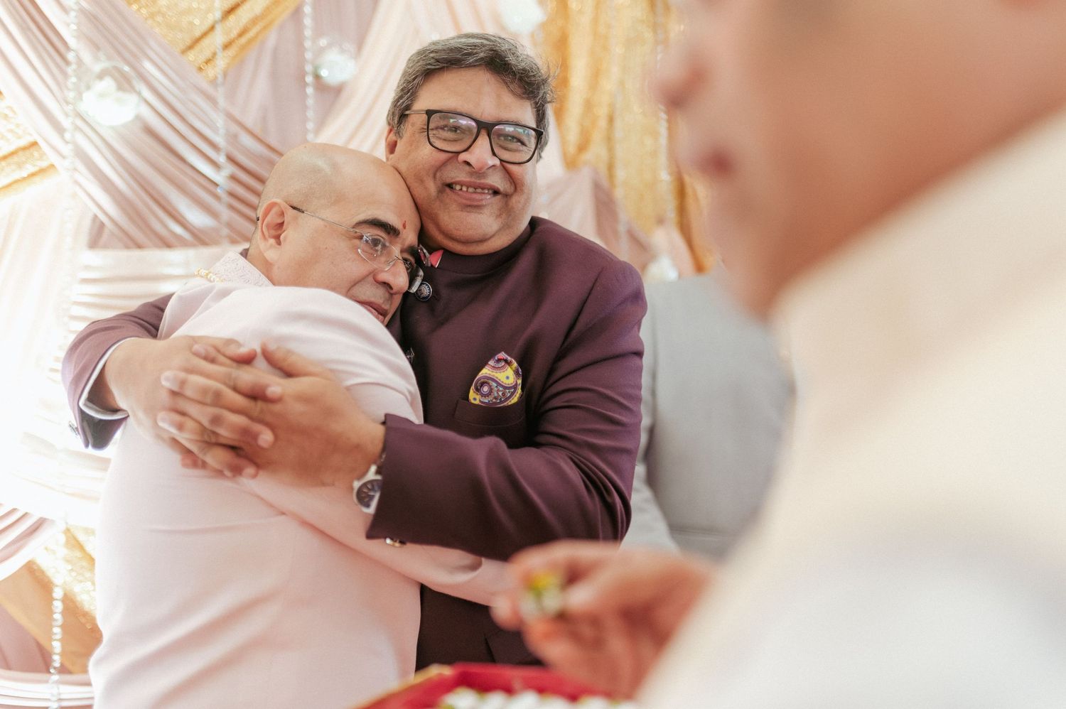 Two men share a warm embrace during a traditional Indian wedding celebration.