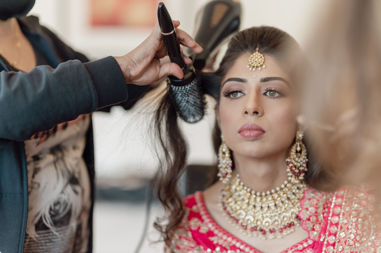 Bride in pink lehenga gets hair styled with gold jewelry and maang tikka for Indian wedding.