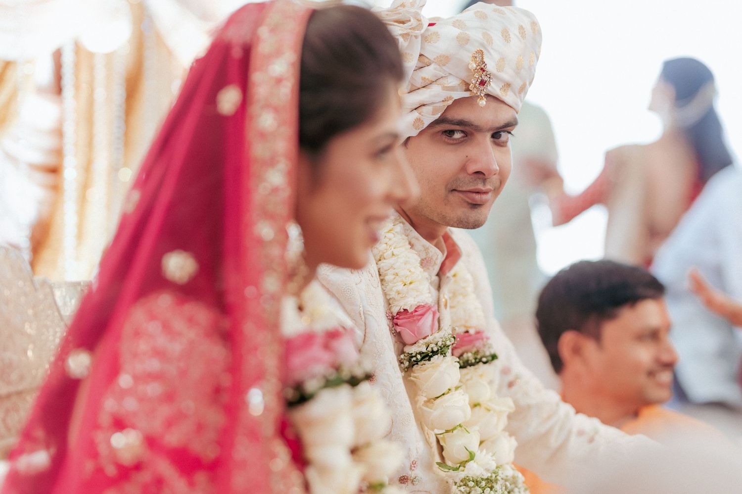 Indian groom in white sherwani and turban with bride during traditional Hindu wedding ritual.