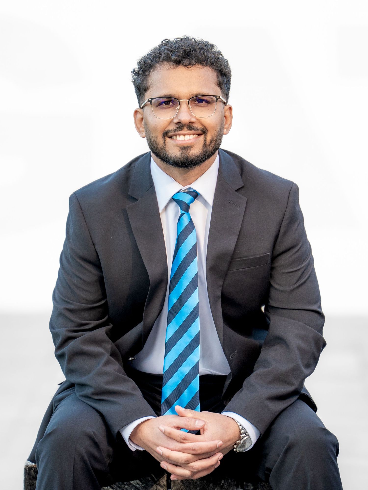Smiling man in dark suit and blue striped tie sits for a professional business headshot.