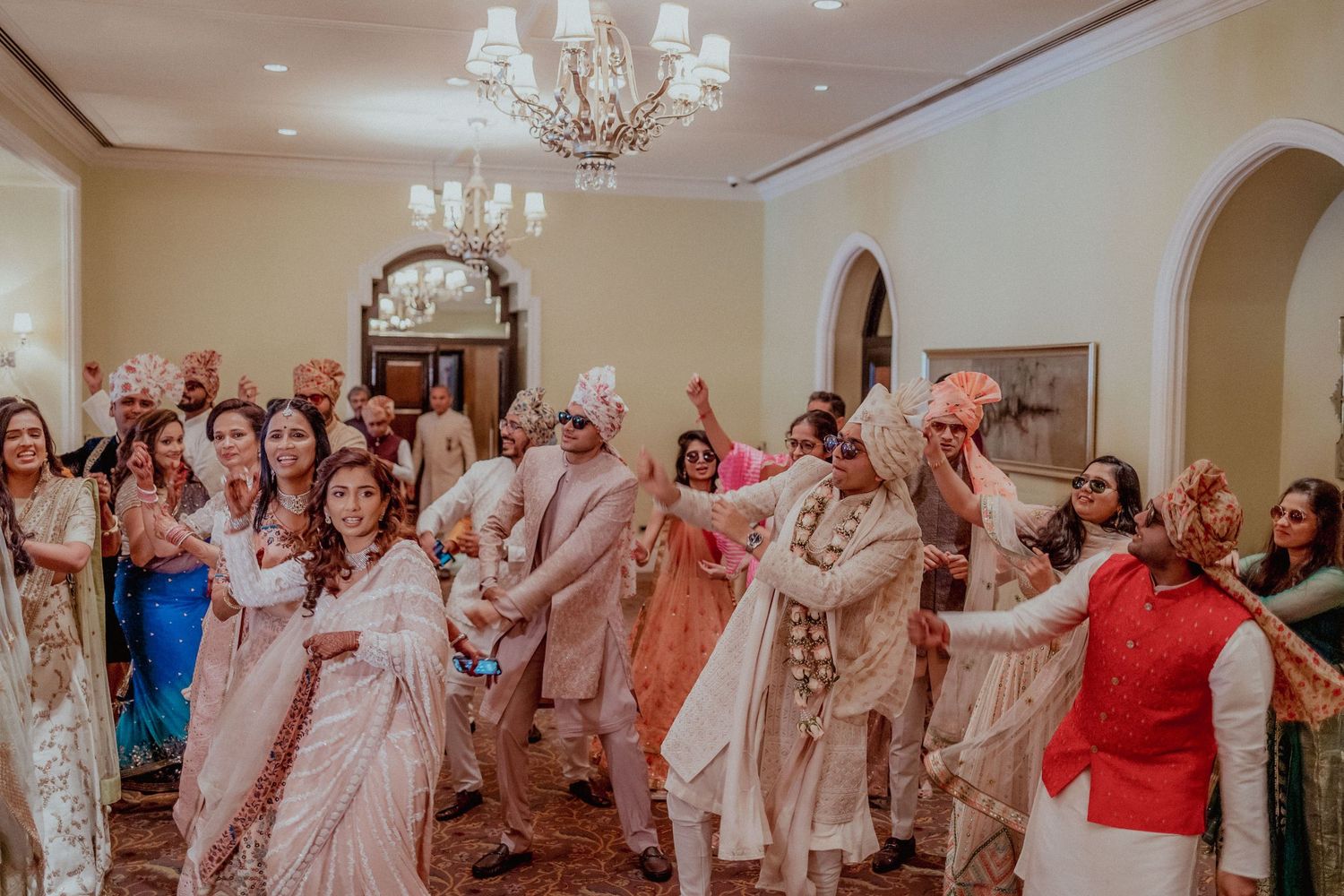 Large group of guests in colorful Indian attire celebrate and dance at a wedding reception.