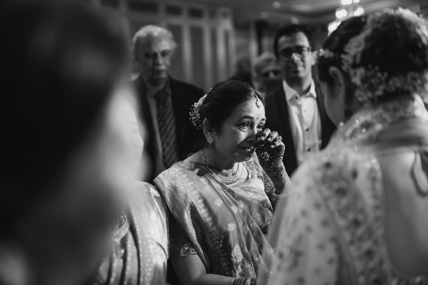 Emotional Indian wedding guest wipes tears during heartfelt ceremony moment captured in black and white.
