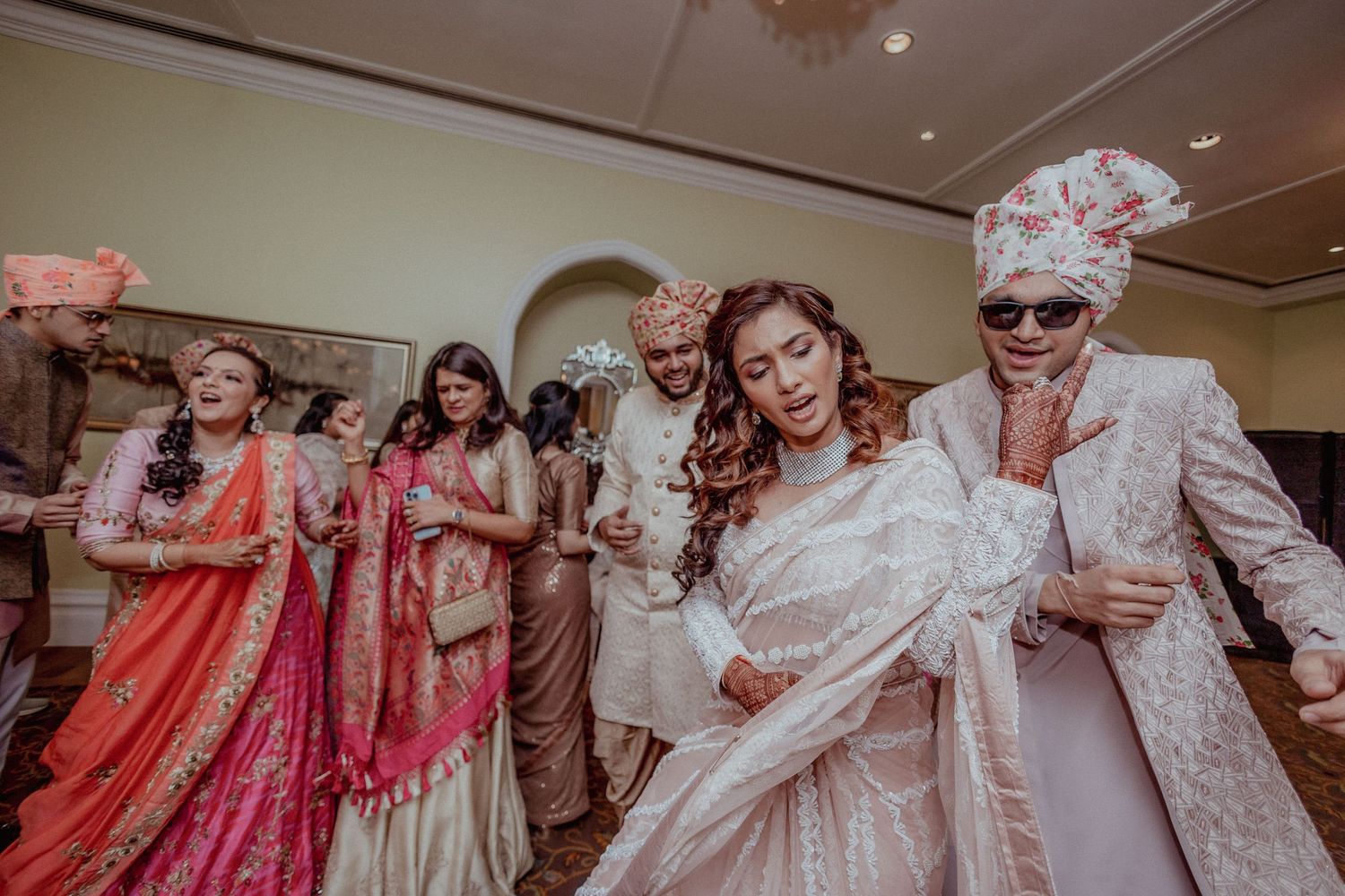Bride and groom in traditional Indian wedding outfits dance together with family members.