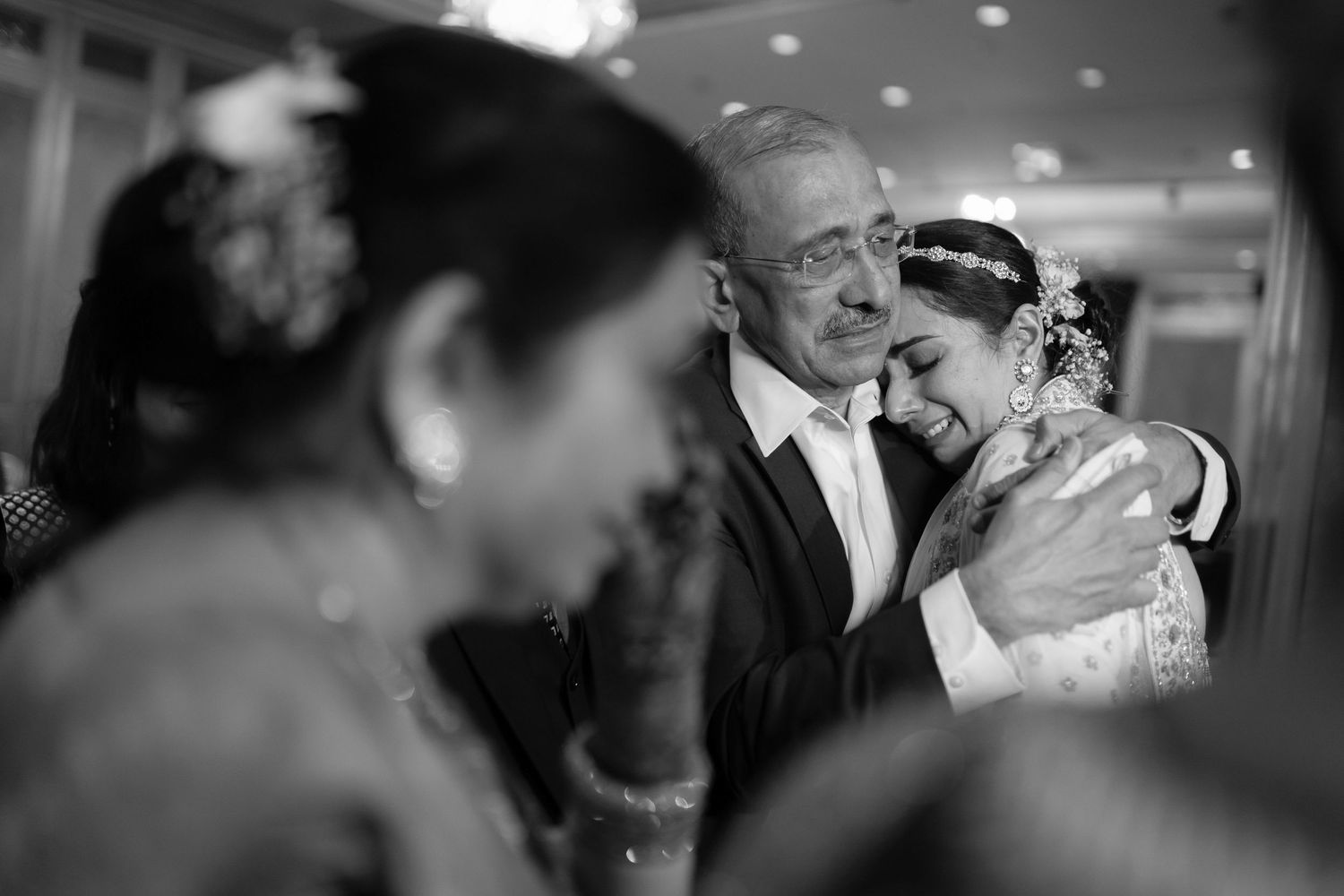 Black and white photo of a bride embracing an older gentleman at a wedding.