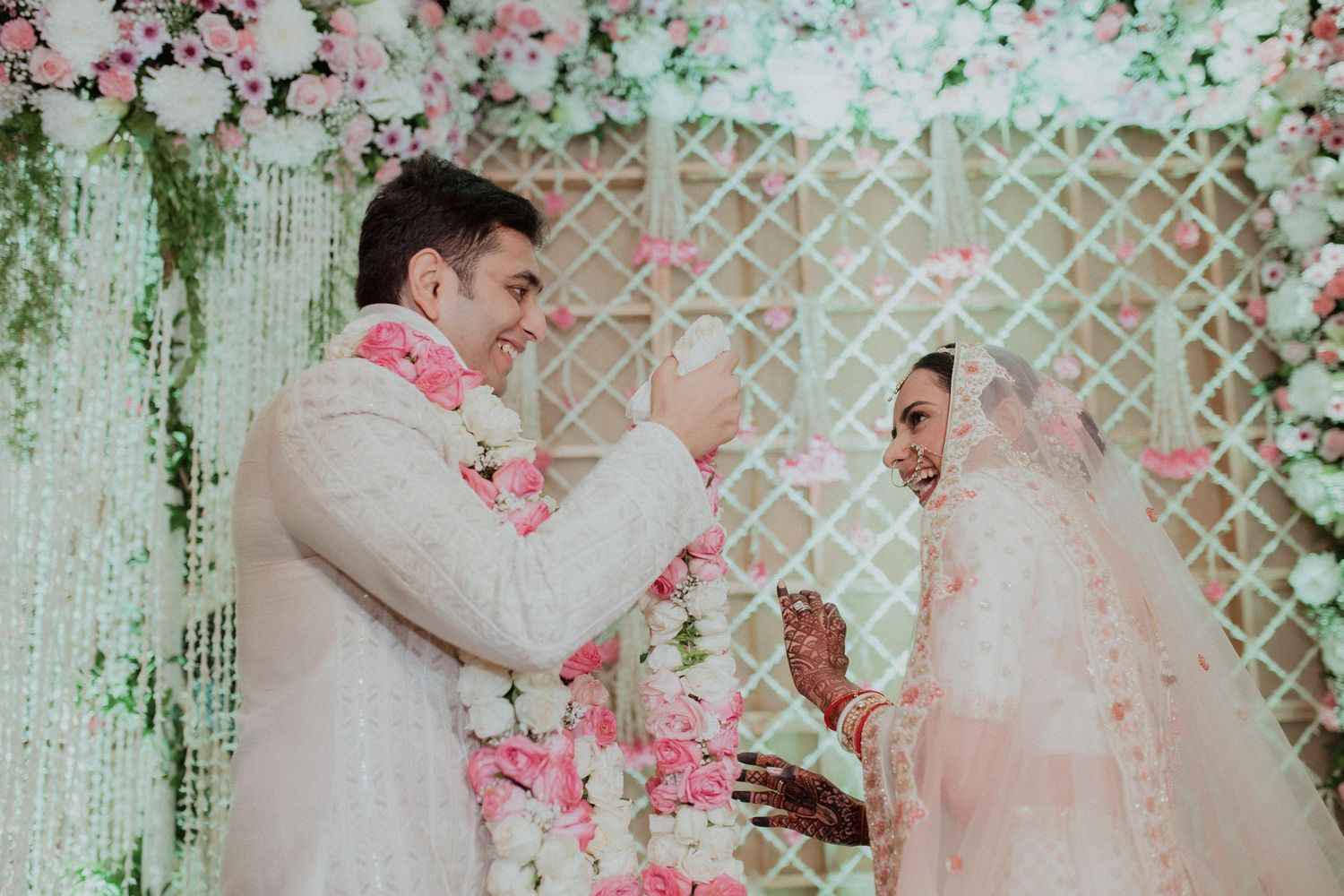 Bride and groom exchanging garlands at a traditional Indian wedding ceremony with pink floral backdrop.