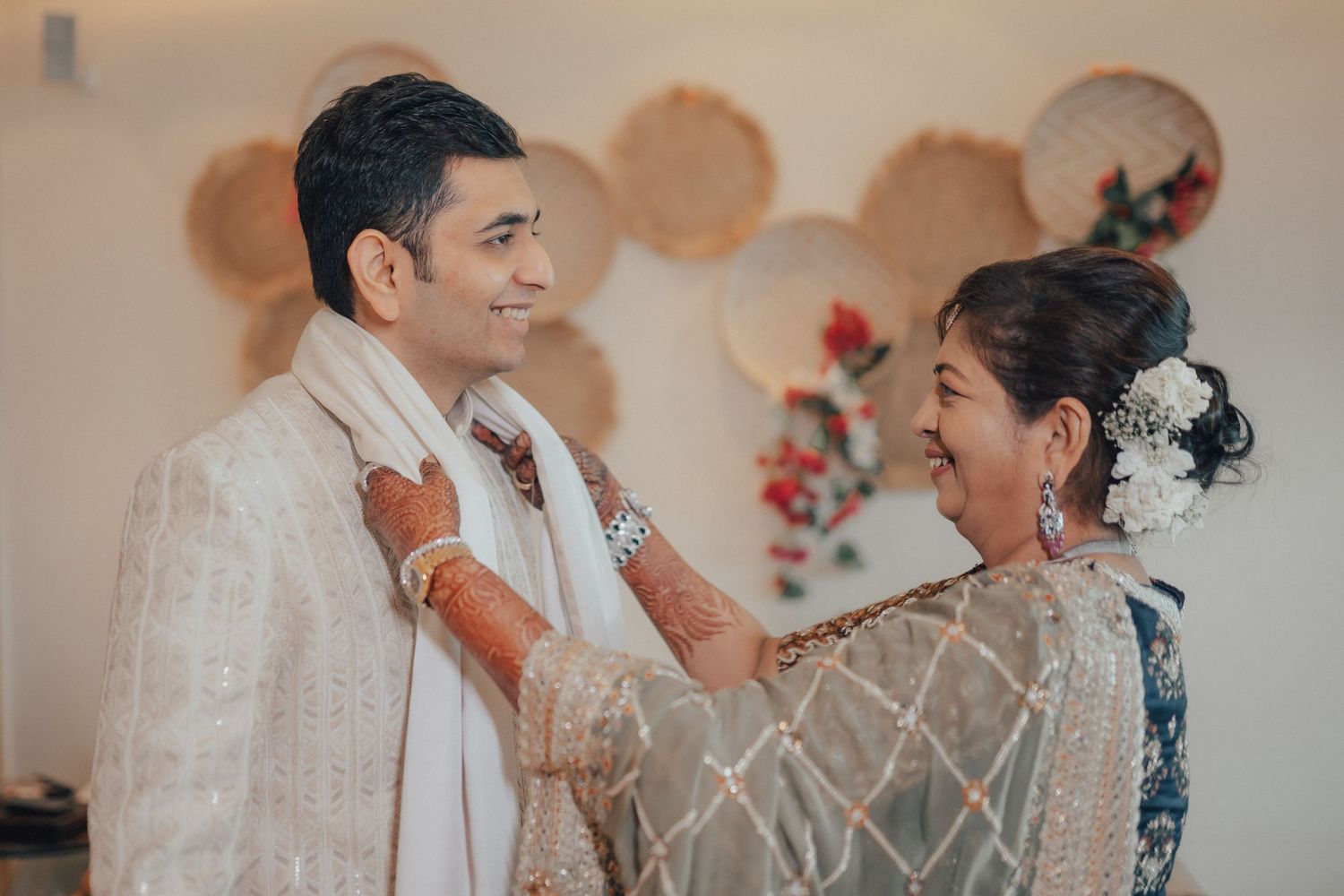 A smiling groom in white sherwani shares a joyful moment with a woman in a grey saree.