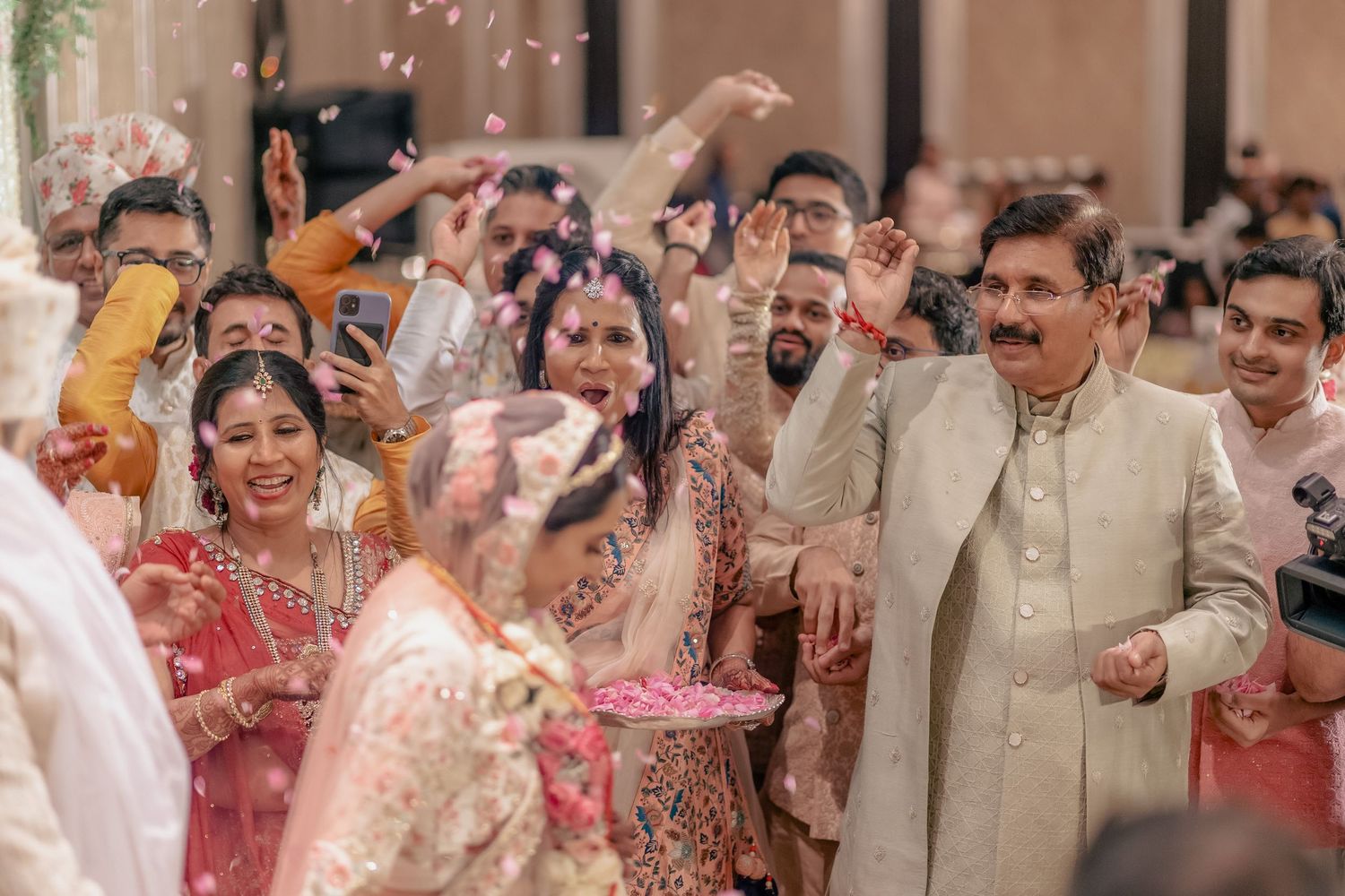 Joyful Indian wedding guests celebrate with flower petals as bride and groom walk by.
