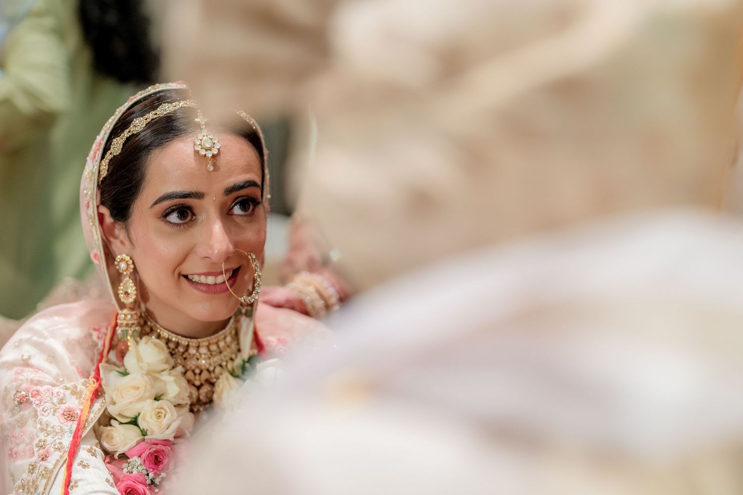 Beautiful Indian bride in pink lehenga with gold jewelry smiles during wedding ceremony.
