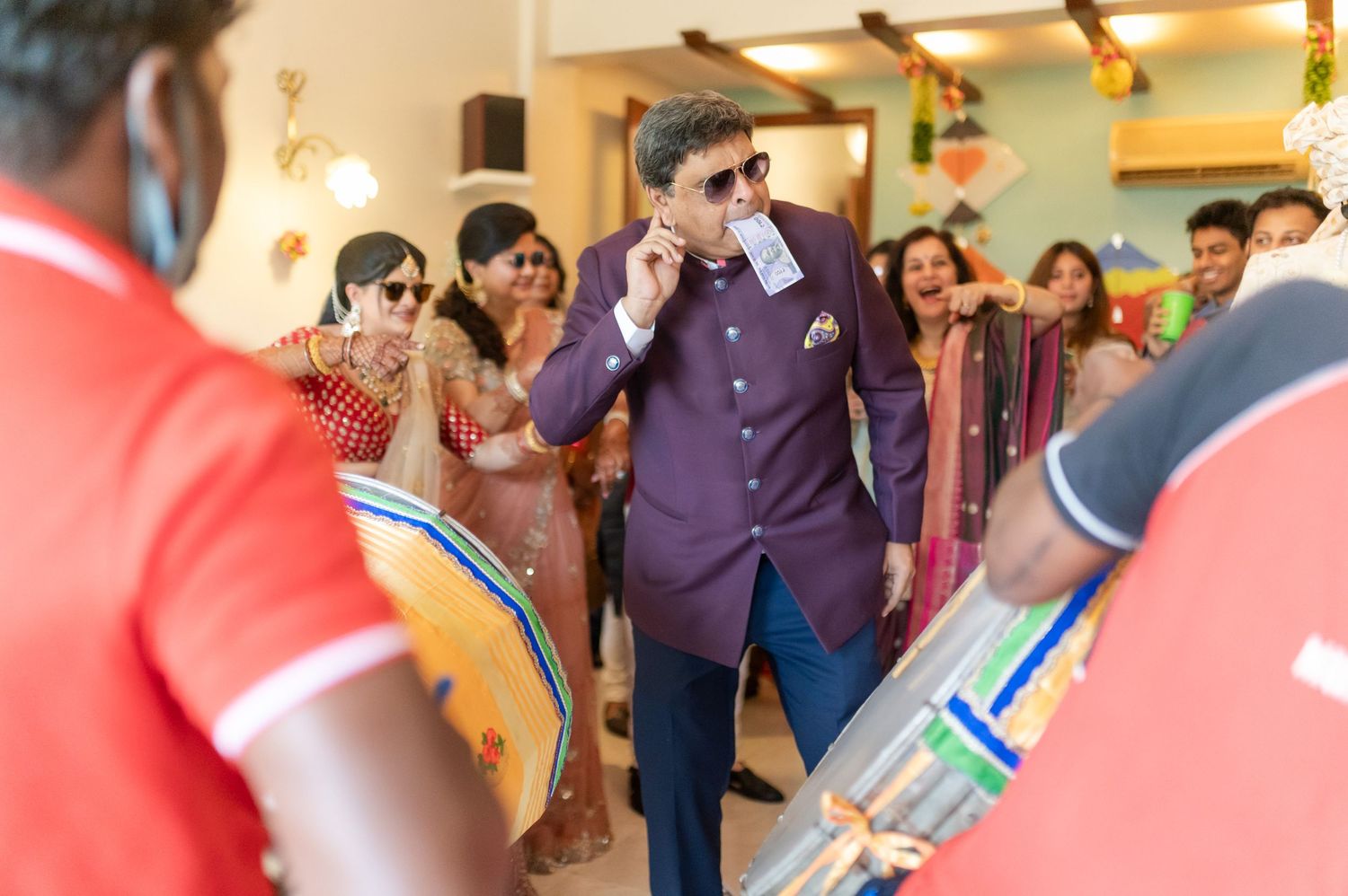 Man in purple suit dancing at Indian wedding celebration with dhol drummers.