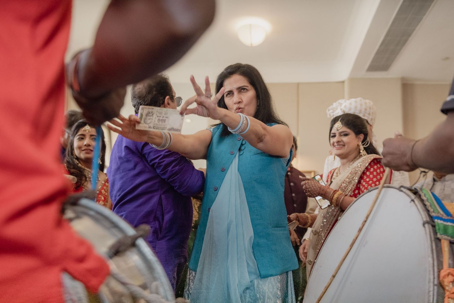 Woman in blue saree dancing expressively near dhol during lively Indian wedding festivities.
