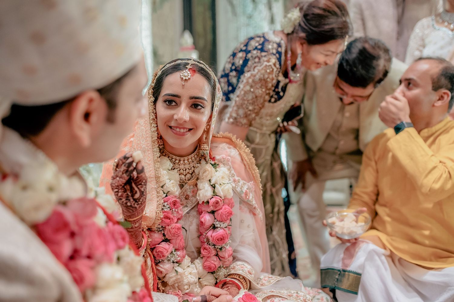 Radiant bride in peach lehenga smiles warmly during traditional Indian wedding ceremony.