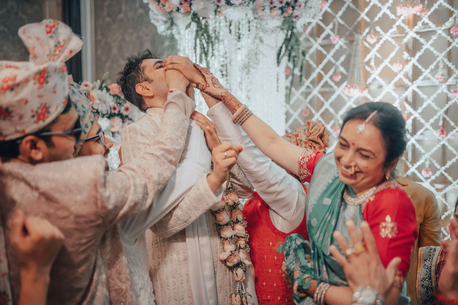 Joyful Indian wedding ceremony with guests placing a floral garland on the groom in traditional attire.