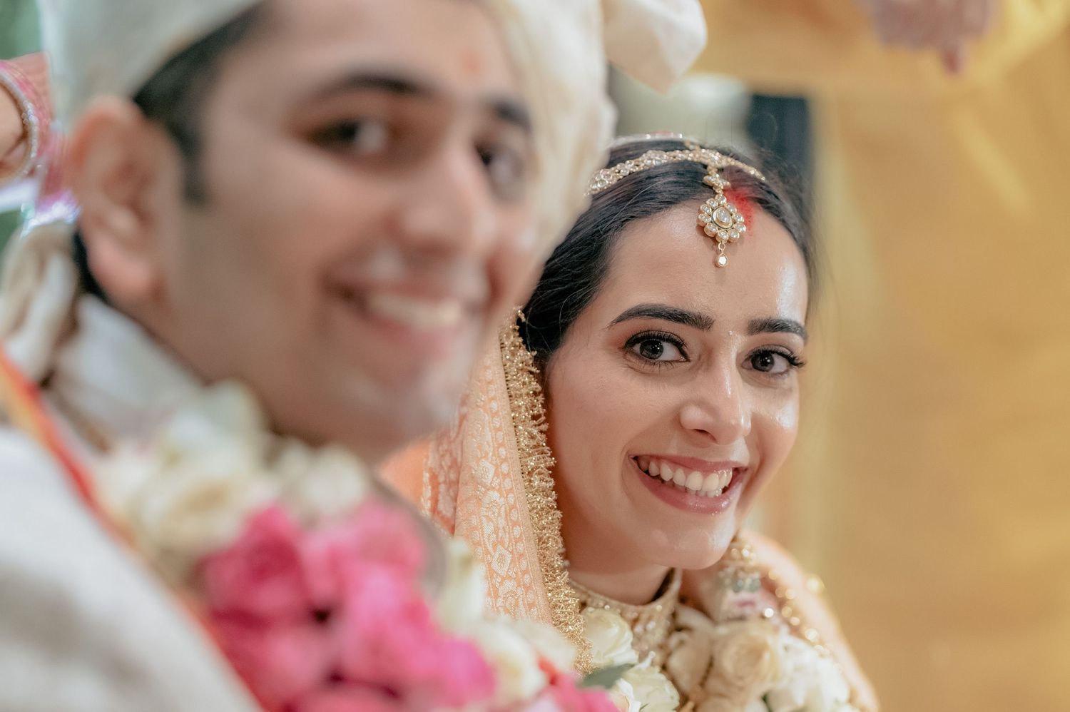 Joyful Indian bride in golden dupatta smiles beside groom during traditional wedding ceremony.
