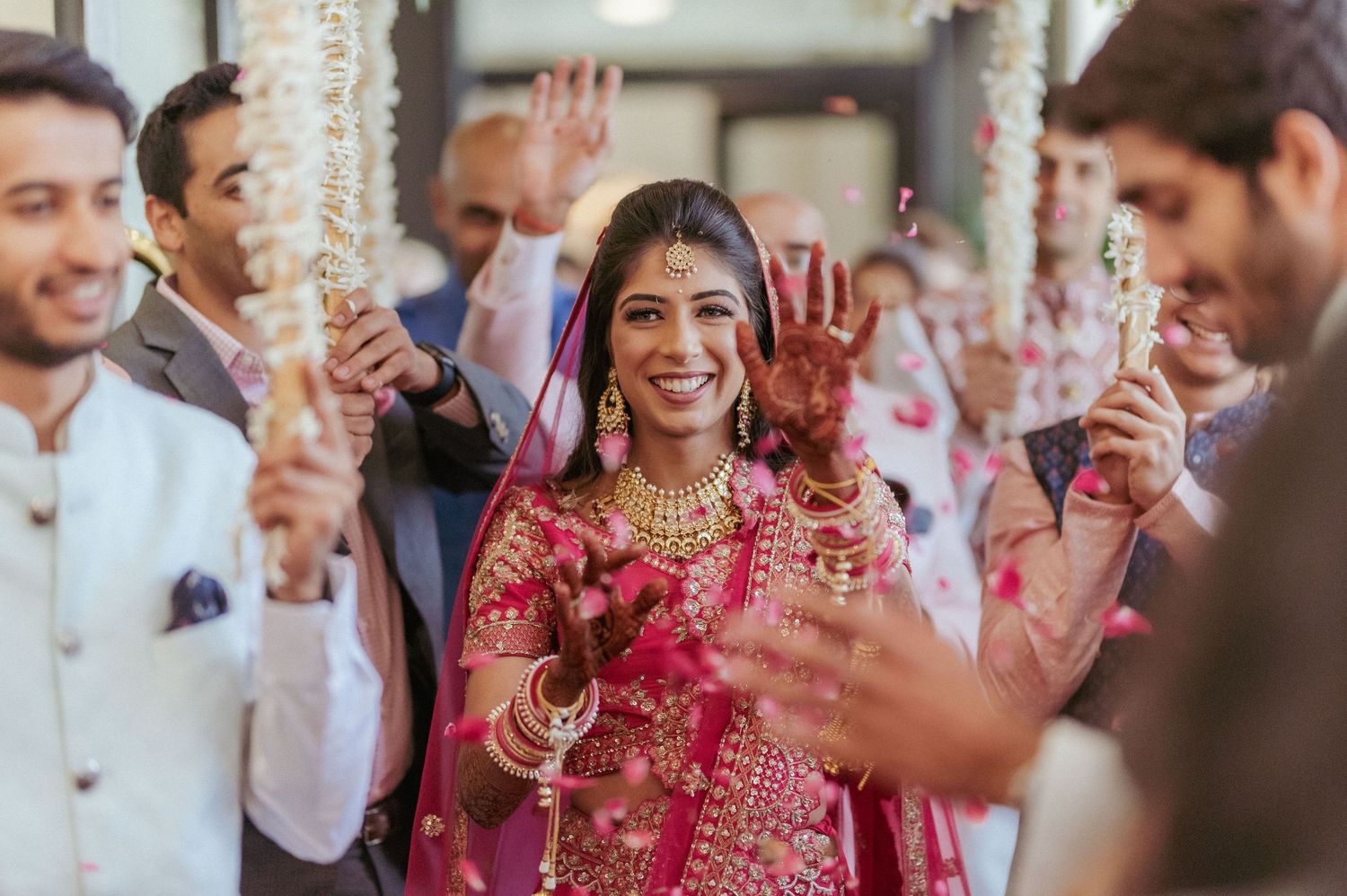 Radiant Indian bride in red lehenga smiles during festive bridal entry at wedding ceremony.