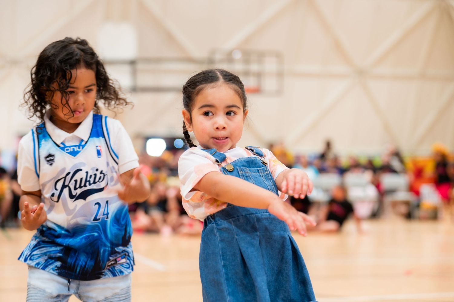 Two young girls in a gymnasium dancing together at a Pacific cultural celebration event.