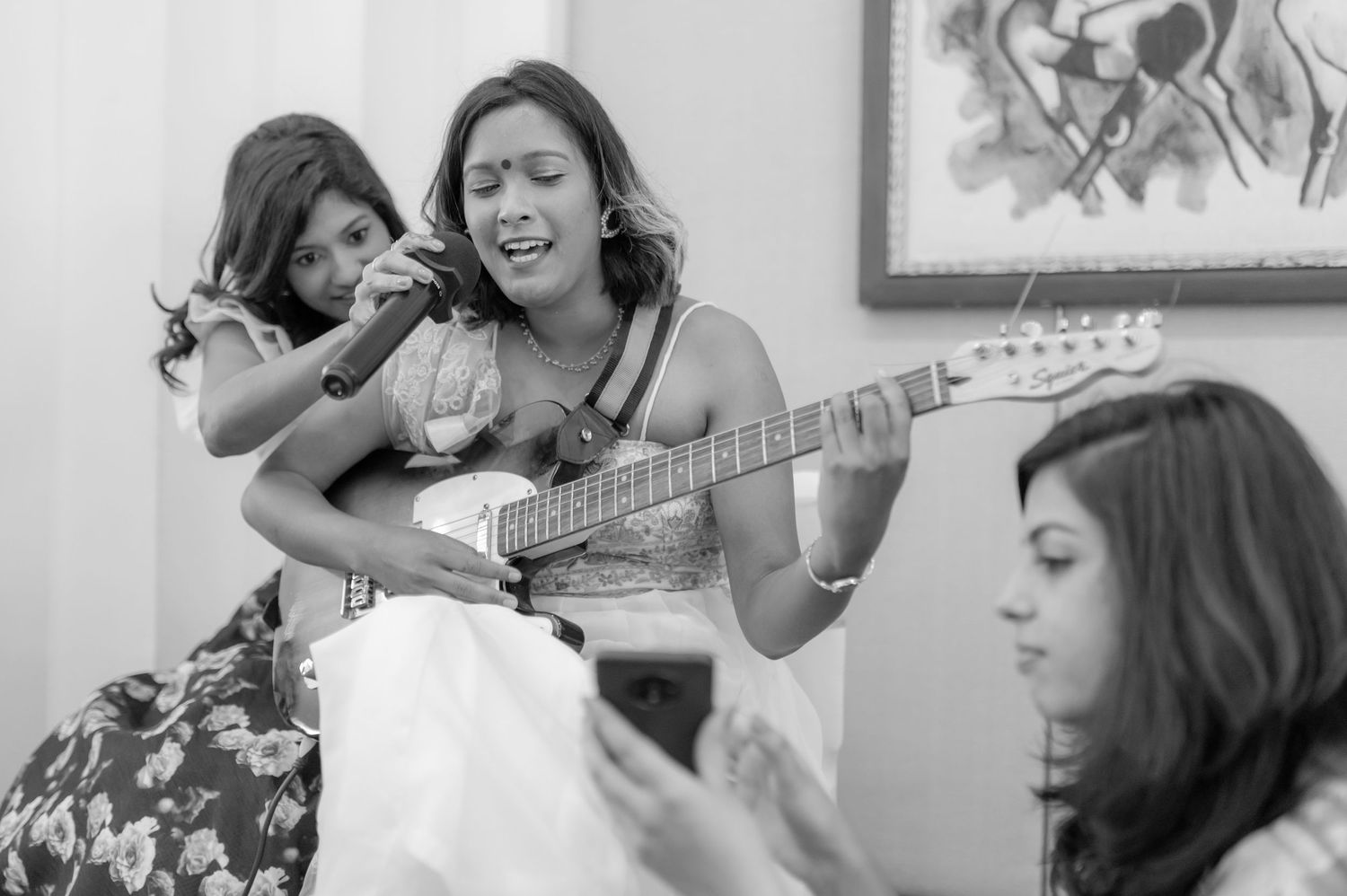Two women playing guitar and singing together at an Indian wedding celebration in black and white.