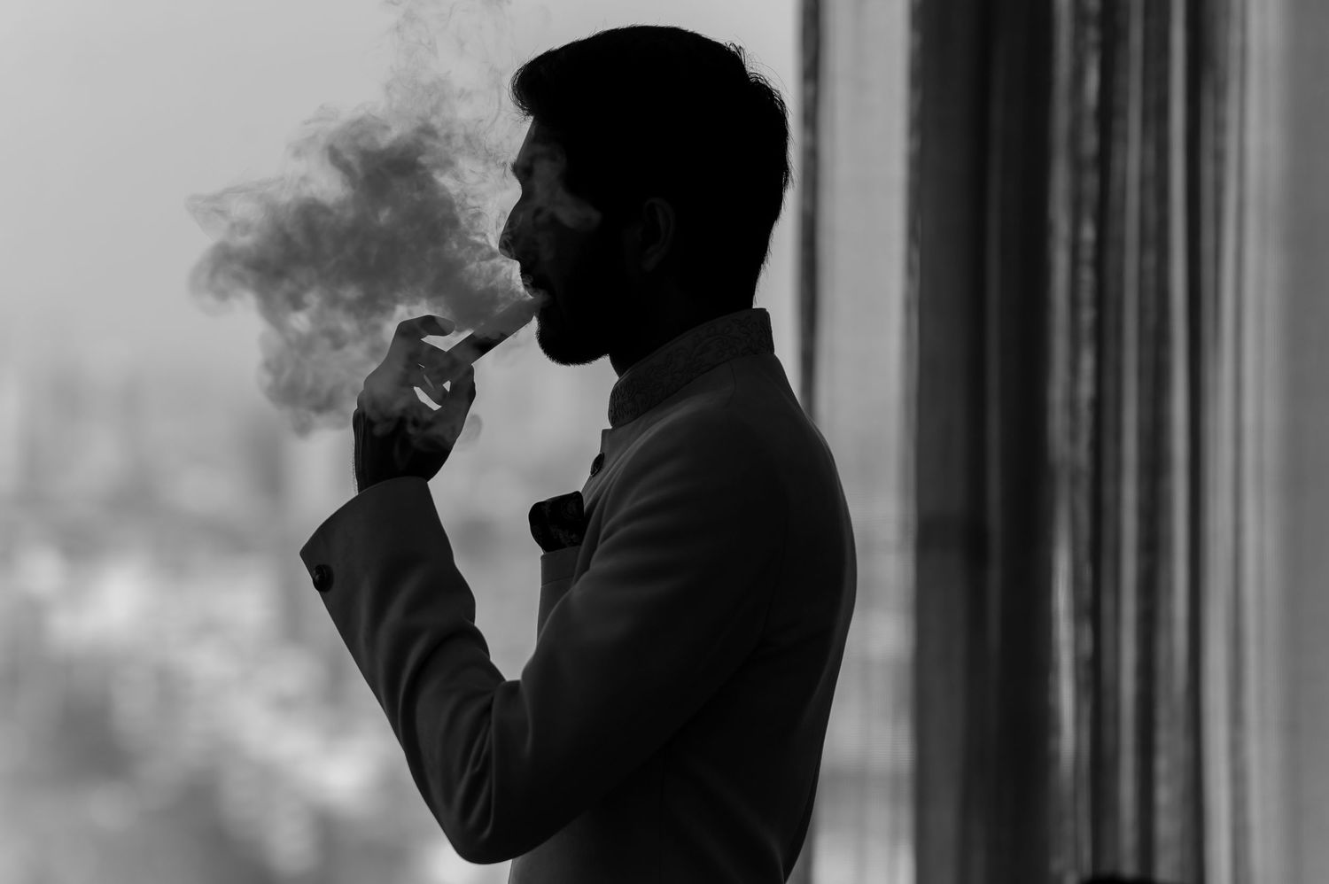 Silhouette of man smoking cigarette by window in black and white.