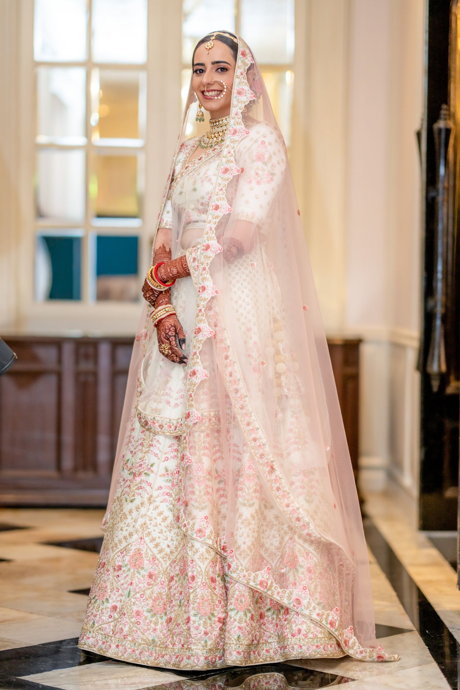 Beautiful Indian bride in embroidered white pink lehenga with dupatta posing in luxury venue.