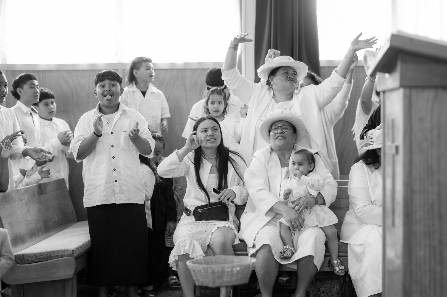Group of people in white attire worshipping with raised hands in church, black and white photo.