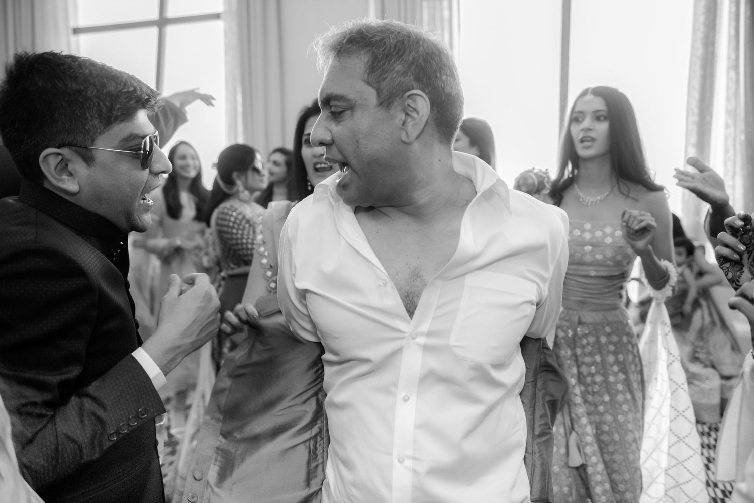 Guests dancing joyfully in black and white photo at an Indian wedding celebration.