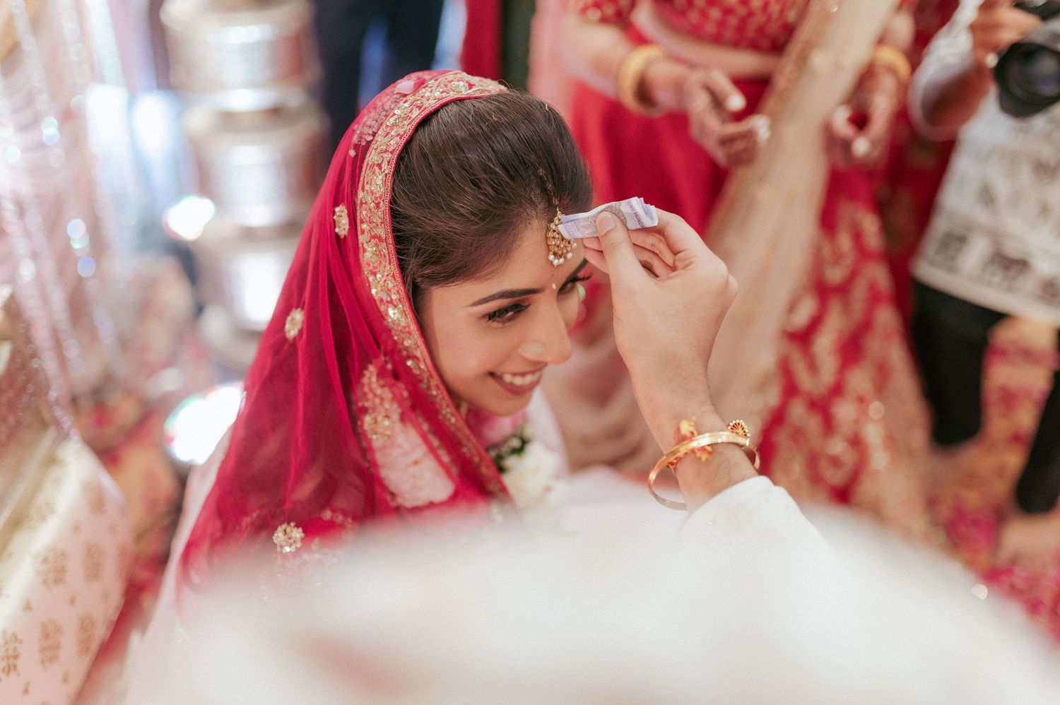 Smiling Indian bride in red bridal lehenga receives sindoor during traditional Hindu wedding ceremony.