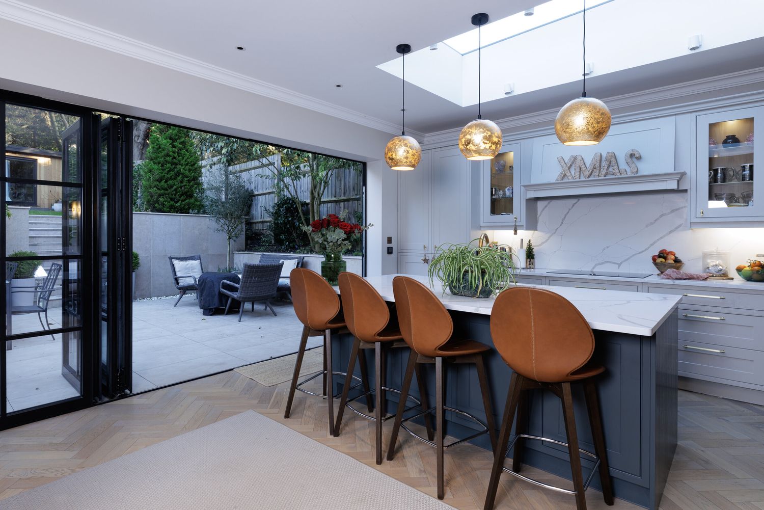 Kitchen island with leather bar stools and pendant lights beneath a rooflight