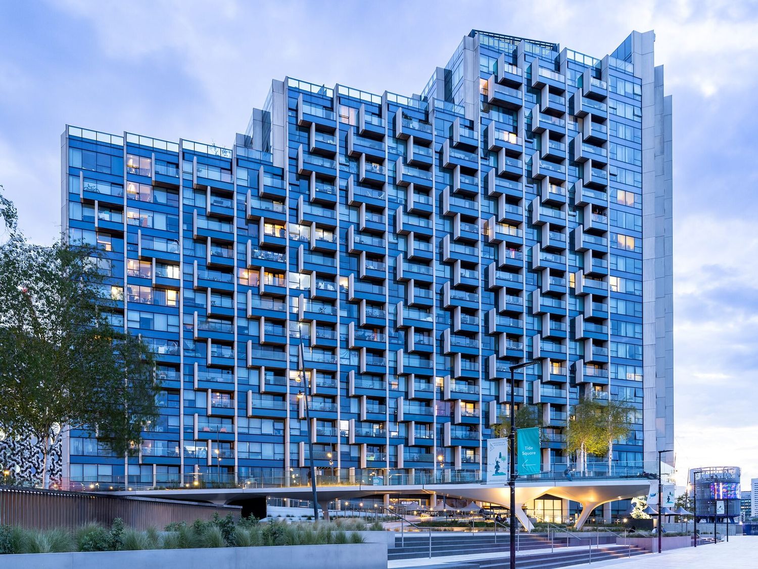 Stepped residential tower with a blue facade at twilight, London
