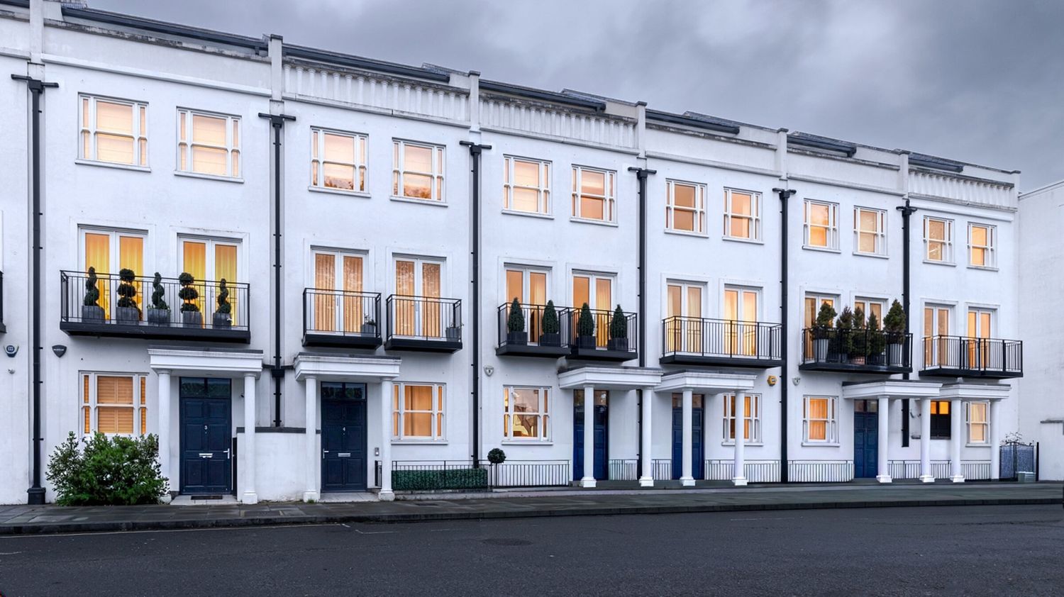 Terrace of white townhouses with lit windows at dusk, London