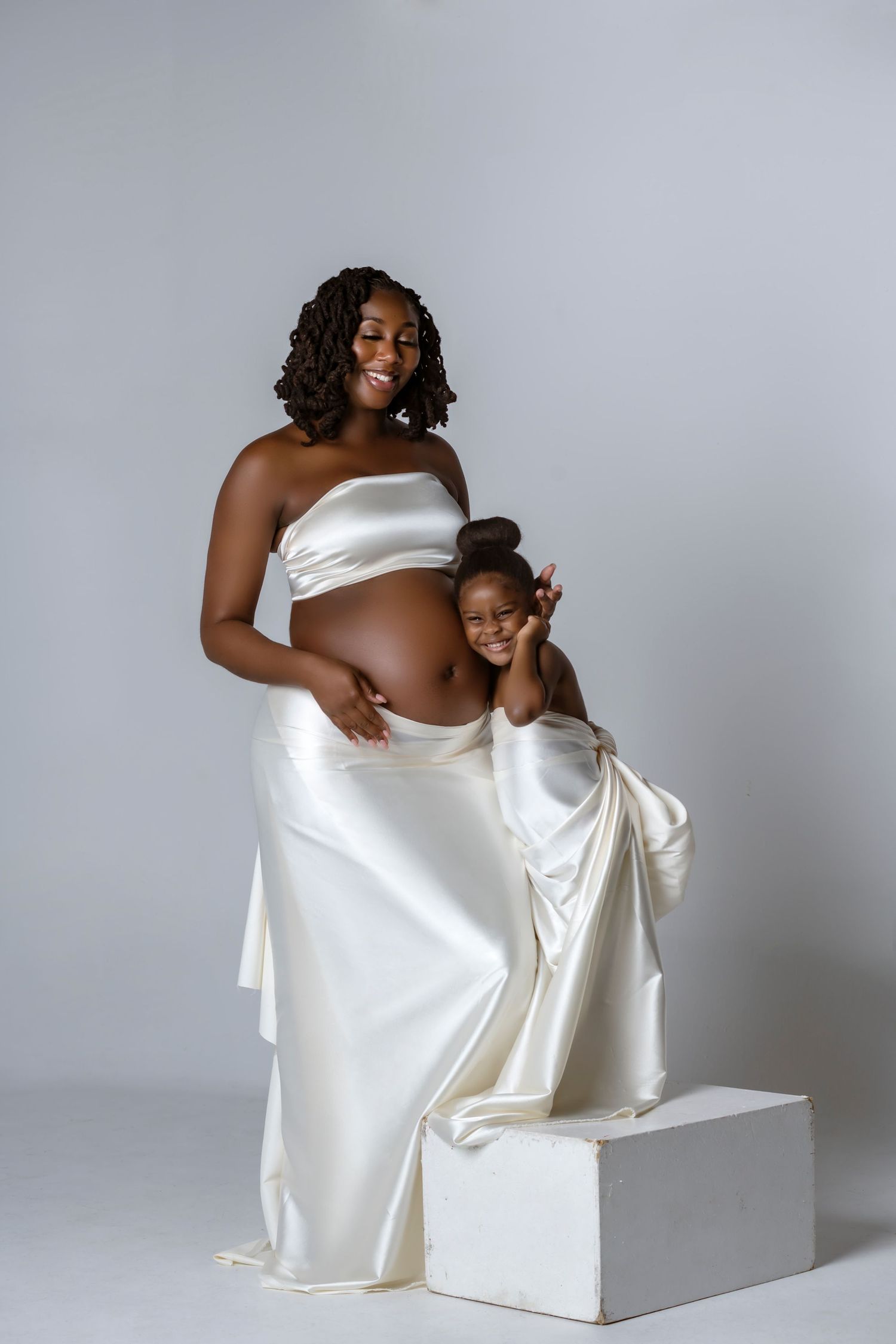 Artistic maternity photo series showing tender moments in white fabric against a light gray backdrop.