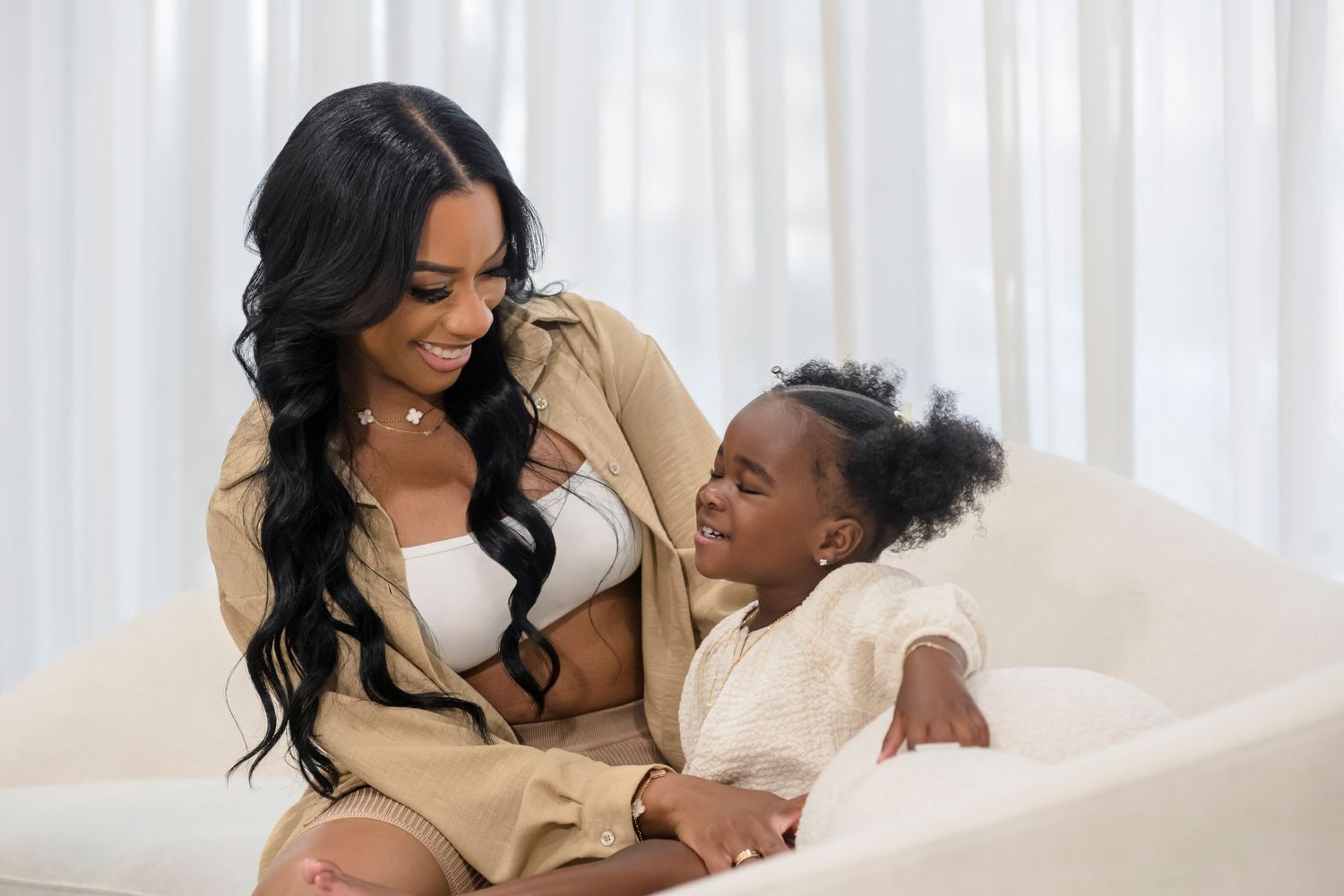 Mother and child sharing playful moment while sitting together on white couch.
