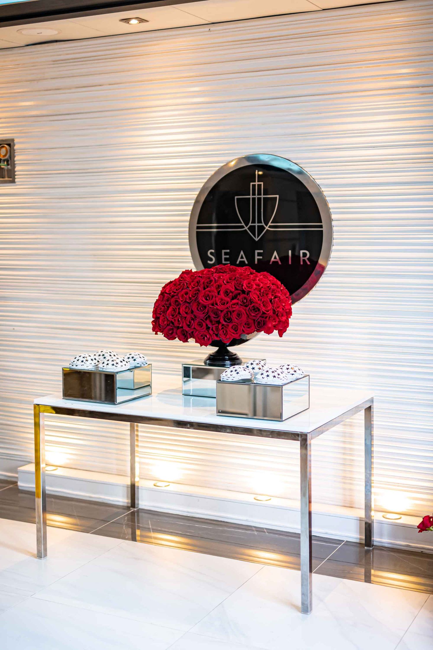 Modern console table with red rose arrangement beneath Seafair logo against textured wall on the Seafair Mega Yacht in Miami.