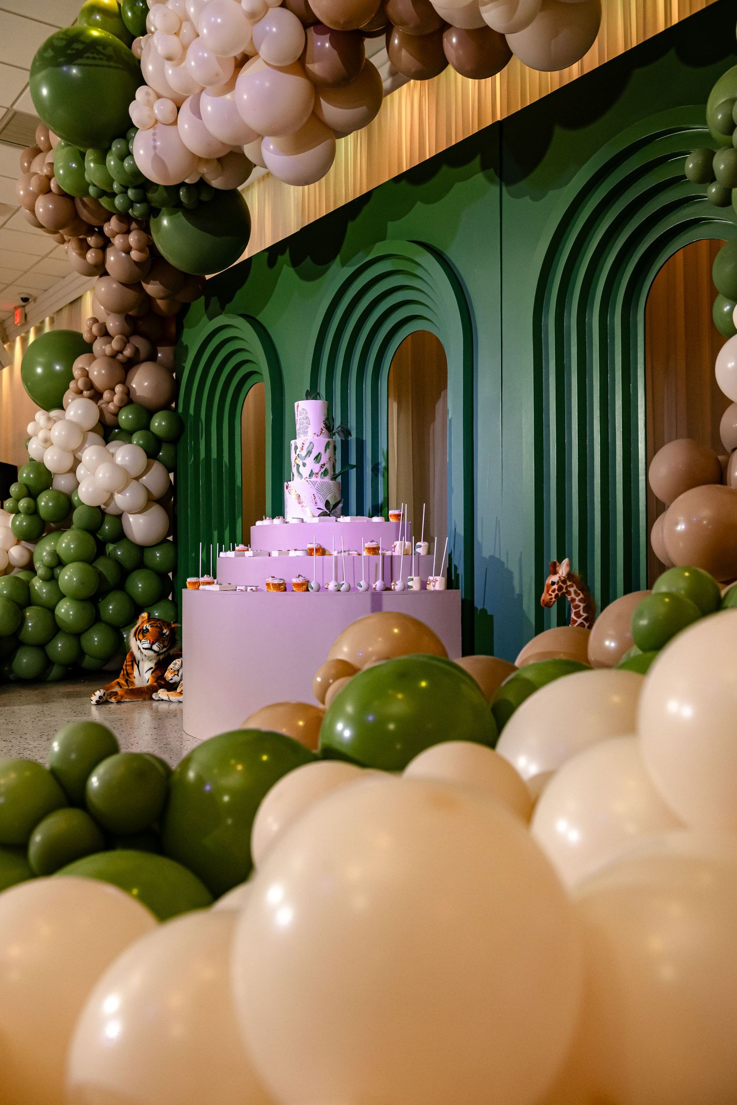 Elegant party setup with green art deco wall panels and cascading white and olive balloon garland decorations.