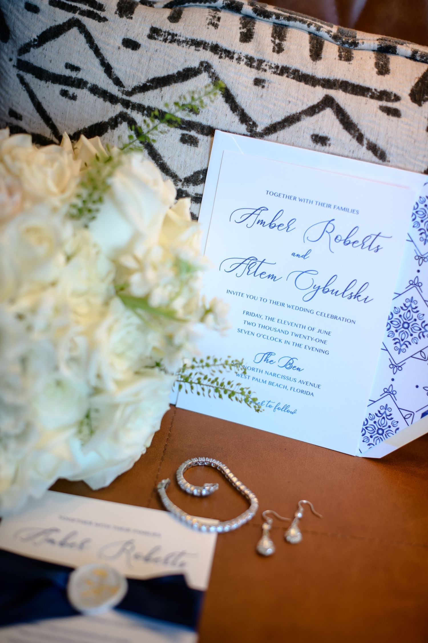 Wedding invitation with blue decorative details alongside white flowers and jewelry.