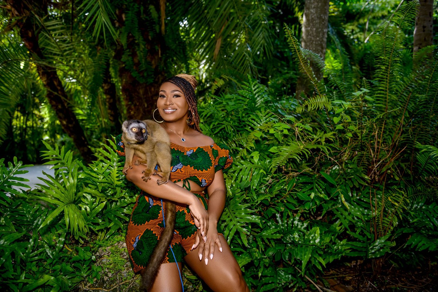 A model poses in a brown bikini surrounded by lush tropical foliage and greenery in a jungle-like setting.