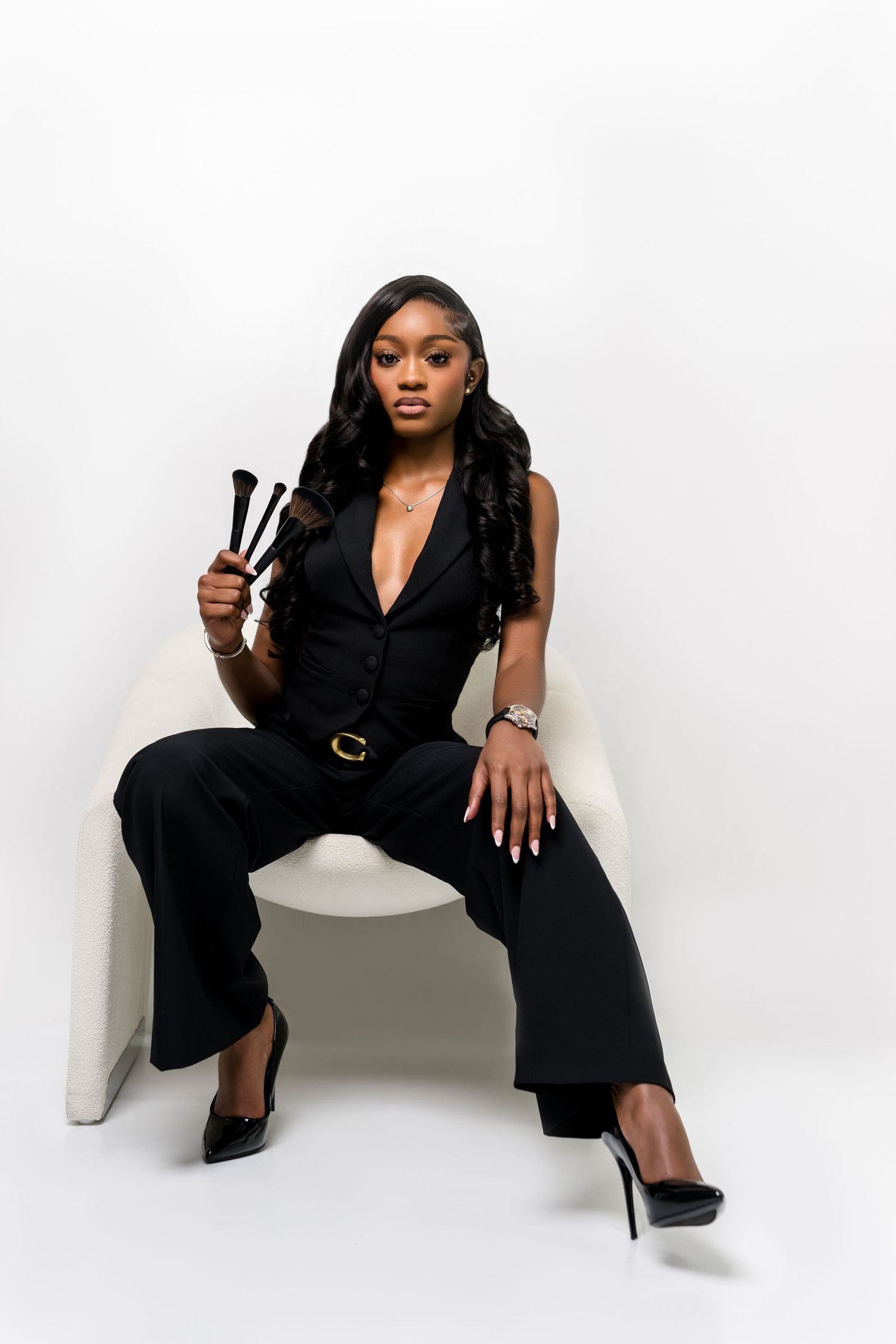 Fashion portrait in black jumpsuit against white backdrop with makeup brushes.