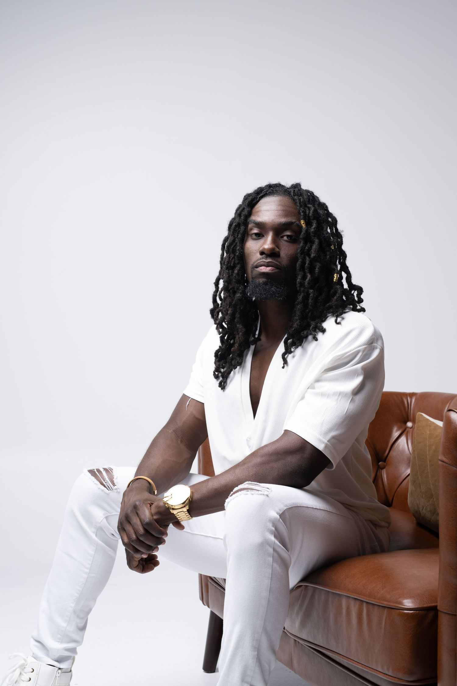 Person in white outfit sitting on brown leather chair in multiple artistic poses against light background.