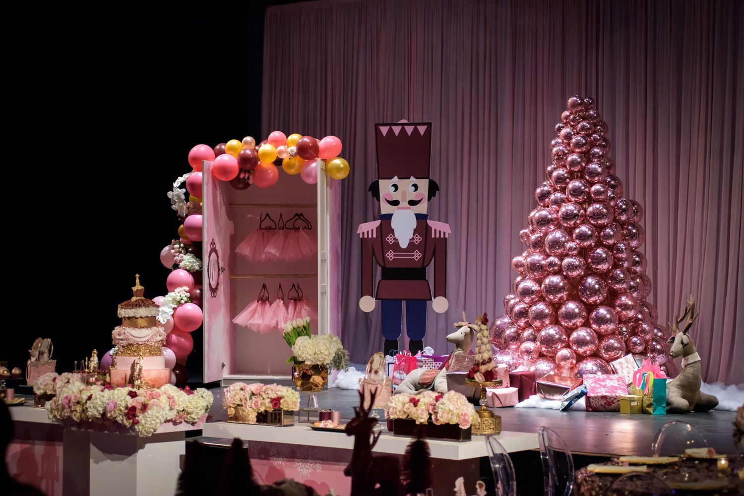 Pink and white holiday dessert display features cupcakes, cakes, and treats arranged on a tiered table with festive decorations.