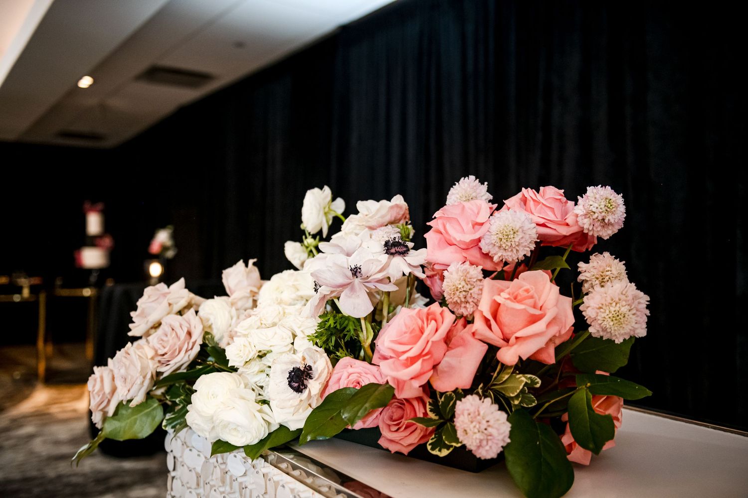 A beautiful floral arrangement of pink and white roses with carnations on a dark surface against a black backdrop.