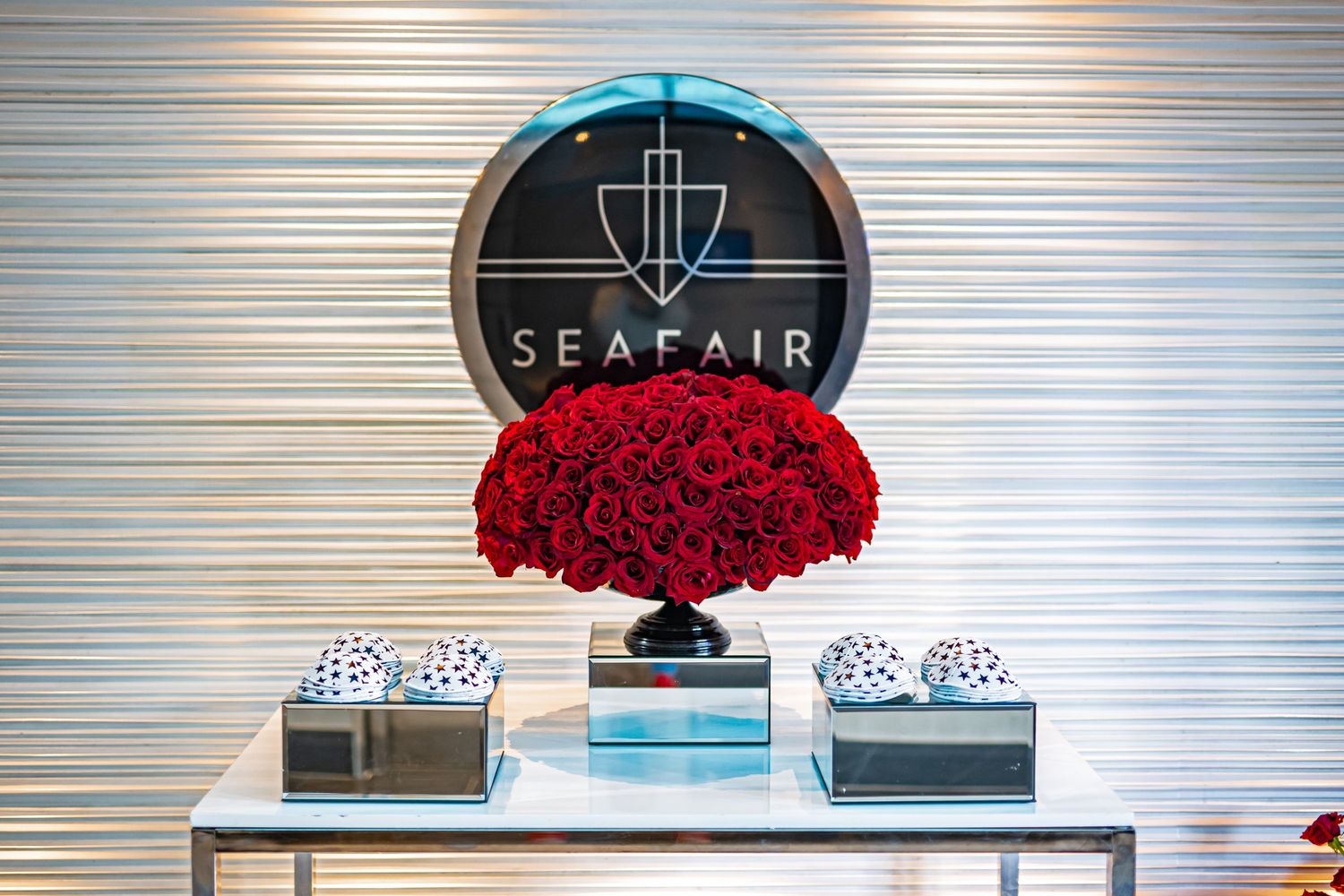 Elegant display featuring a Seafair logo sign with vibrant red roses in a black vase and decorative boxes on a table.