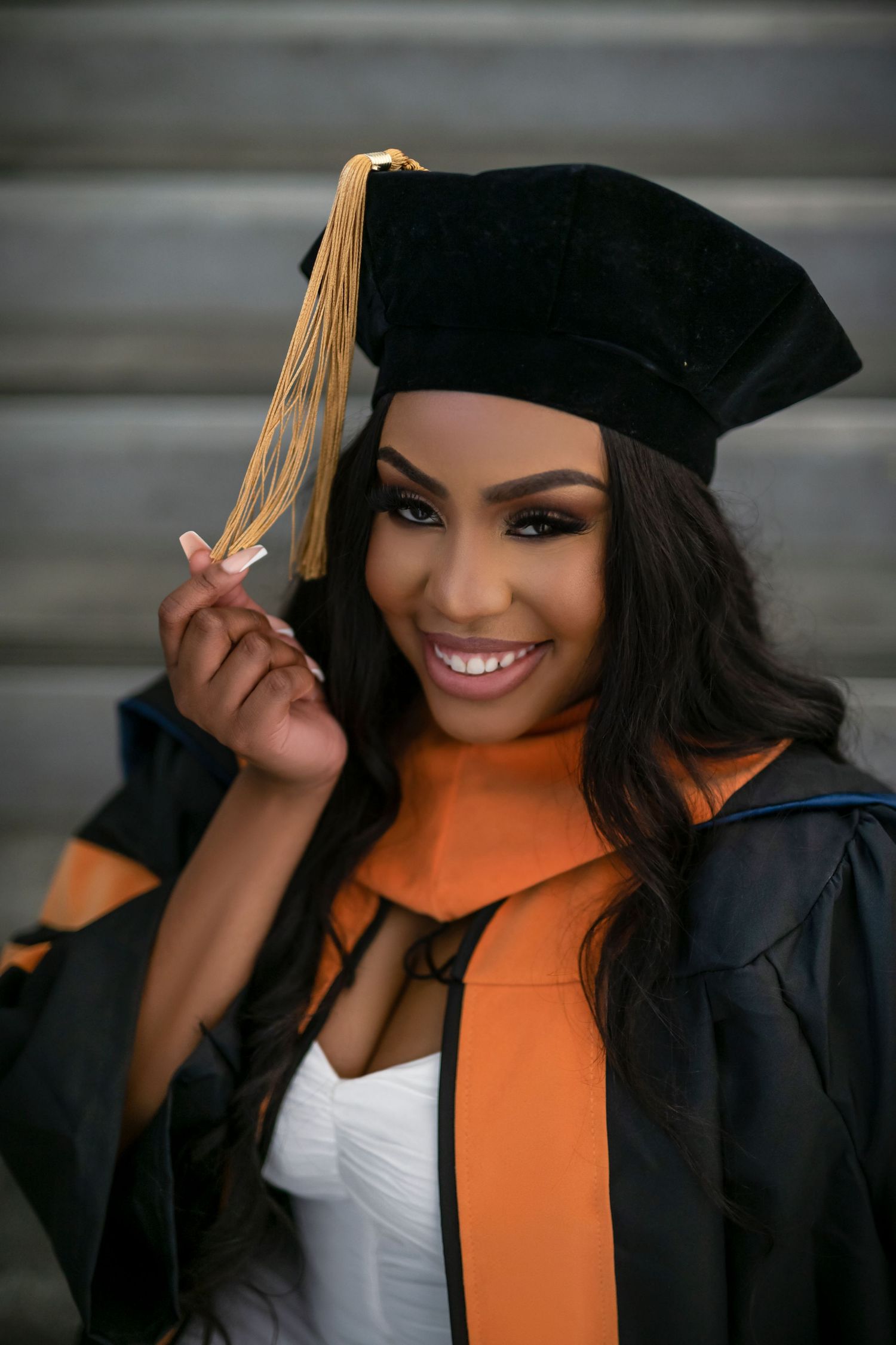 Graduate wearing black cap and gown with orange stole poses for a series of celebratory graduation photos.
