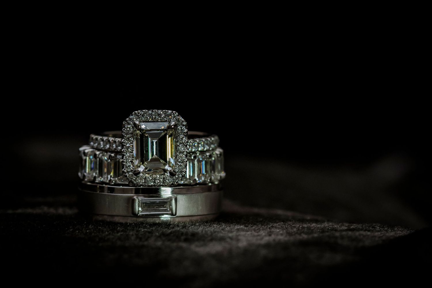 Stunning emerald cut engagement ring with diamond halo on dark background.