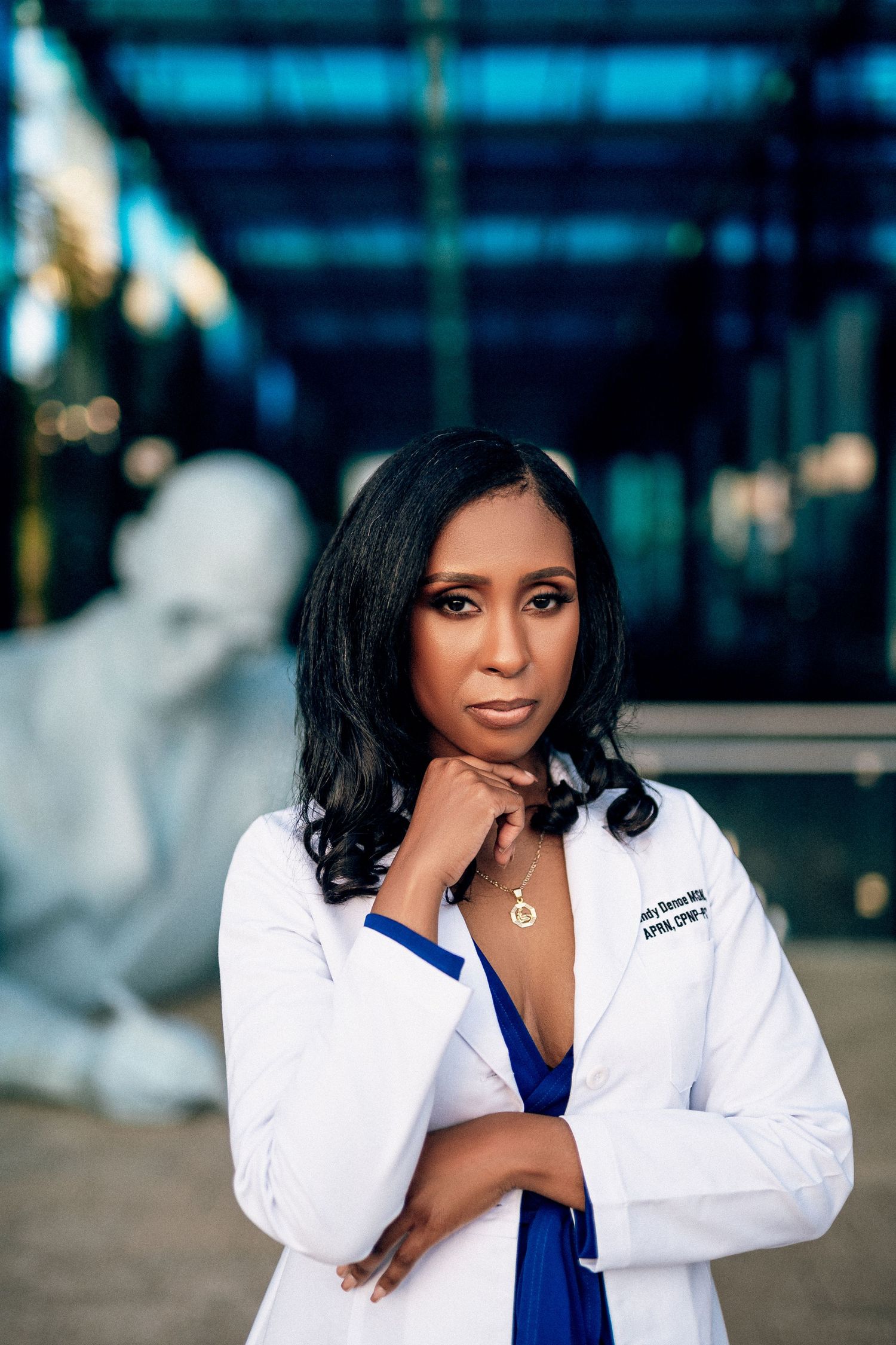 Professional wearing a white lab coat and blue top poses confidently against a blurred city background.
