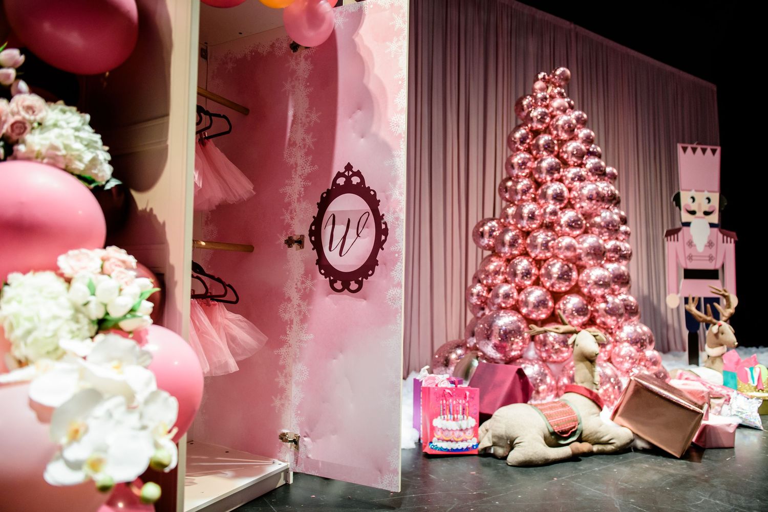 A pink-themed Christmas display with decorated trees, ornaments, and white floral arrangements in an elegant setting.