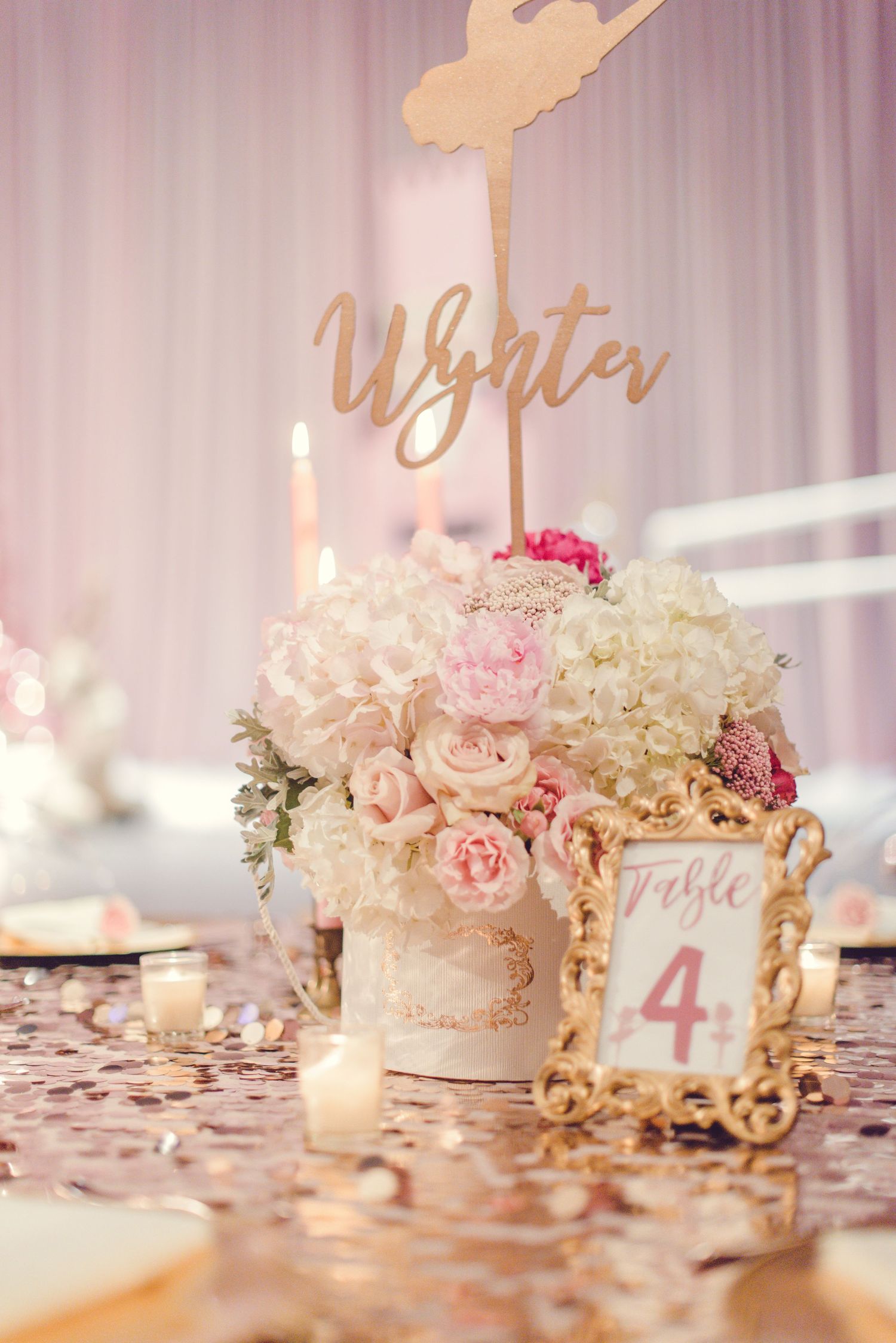 Romantic table setting with gold frames, pink roses, and candlelight against a soft white backdrop.